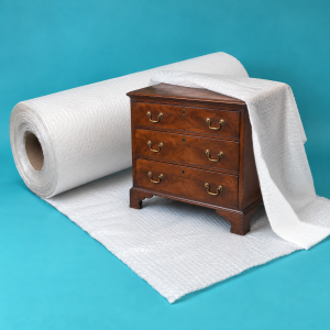 White export bubble blanket roll beside an antique wooden chest of drawers, with the blanket draped over its top and side.
