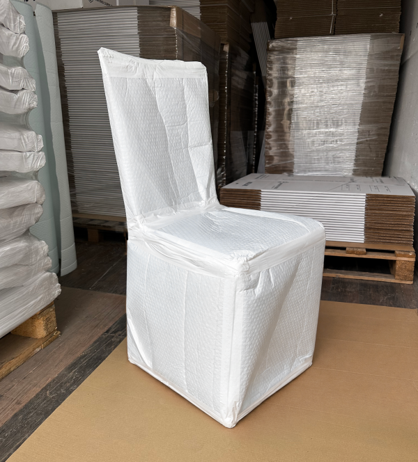 Dining chair fully wrapped in white export bubble blanket, showing the protected backrest, seat and legs in a packaging warehouse.